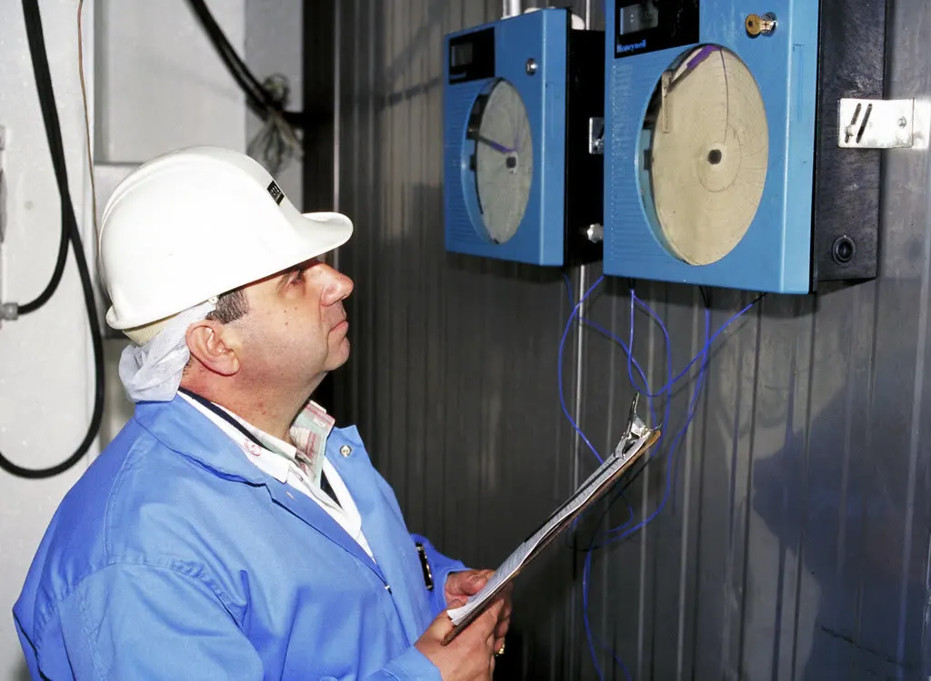 Food safety inspector with a clipboard checking temperature chart recorders