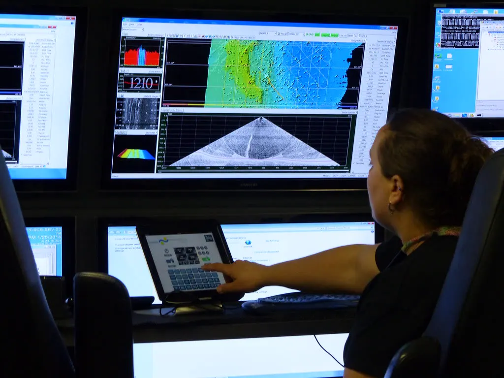 Operator working at a multi-screen data console with a tablet